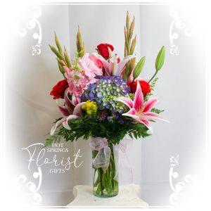 An arrangement of mixed flowers in a vase, featuring lilies and hydrangeas, with a decorative ribbon, presented against a patterned backdrop.