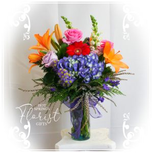Colorful floral arrangement in a glass vase featuring a mix of blooms such as lilies, gerberas, and hydrangeas.