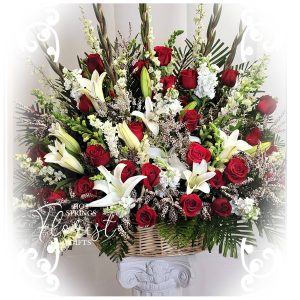 A lavish floral arrangement featuring red roses and white lilies in a basket.