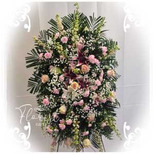 An elegant floral arrangement with pink roses, lilies, and assorted greenery displayed against a white backdrop.