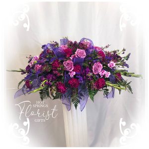 A lavish floral arrangement with purple and pink flowers adorned with ribbons, displayed by a florist.