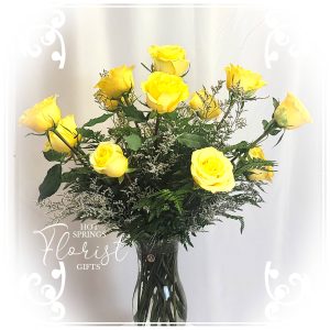 A bouquet of yellow roses with greenery in a vase.