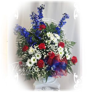 A decorative floral arrangement featuring blue, red, and white flowers with green foliage, presented in a white vase.