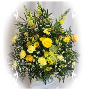 A vibrant floral arrangement featuring yellow roses, lilies, and assorted greenery in a white vase.