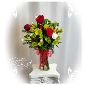 A Holiday Premium Seasonal Bouquet featuring red roses and yellow blooms in a clear vase, set against a white backdrop with a watermark from "hot springs florist & gifts".