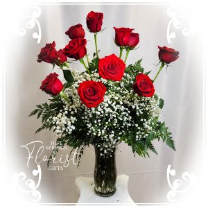 A bouquet of "The Sweetheart" 12 Red Roses Bundle accented with baby's breath and greenery in a glass vase.