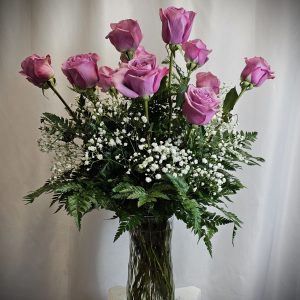 A bouquet of purple roses paired with baby's breath and green foliage in a glass vase.