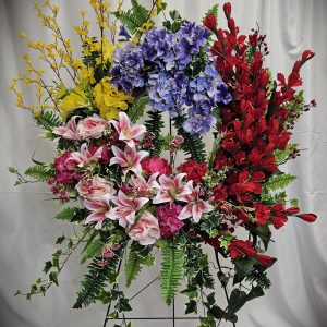 An ornate floral arrangement featuring a colorful mix of yellow, blue, red, and pink flowers with green foliage on a stand.