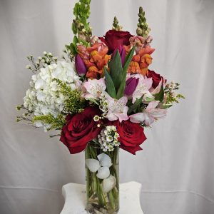 An elegant bouquet of red roses, pink lilies, snapdragons, and white hydrangeas in a clear glass vase.