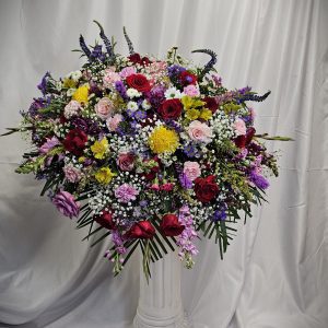 A large, colorful floral arrangement on a white pedestal with a draped background.