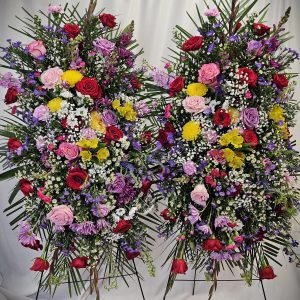 Two large, symmetrical floral arrangements featuring a mix of colorful roses and assorted blooms against a white backdrop.
