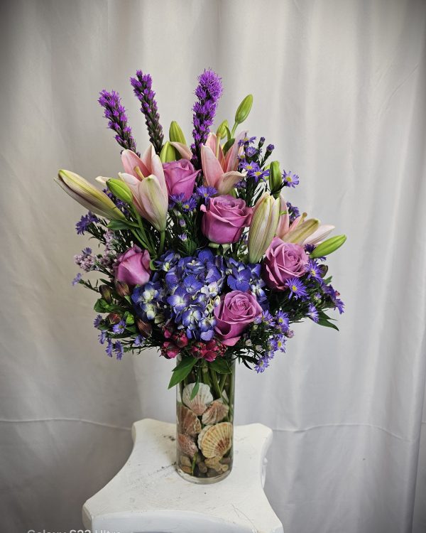 An elegant Cool Water Rose Vase with purple lilies, roses, and hydrangeas in a vase, accented by smaller blue and pink flowers.