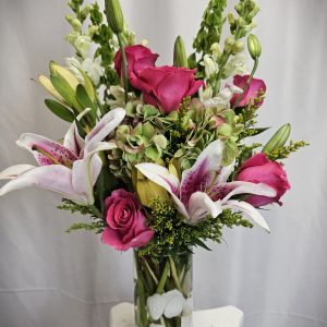 A bouquet of mixed flowers, including lilies and roses, arranged in a clear glass vase.