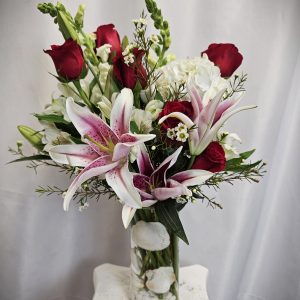 A vivid bouquet featuring Freedom roses and pink lilies in a glass vase, accented with white flowers and greenery.