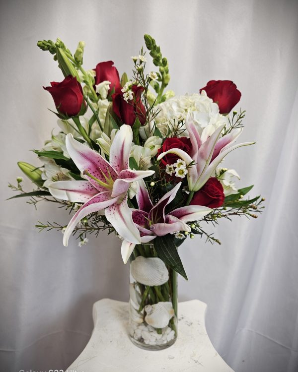 A vivid bouquet featuring Freedom roses and pink lilies in a glass vase, accented with white flowers and greenery.