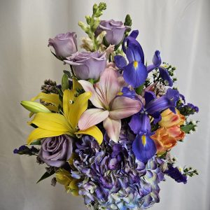 A vibrant floral arrangement featuring a mix of purple, yellow, and blue blooms in a decorative vase.