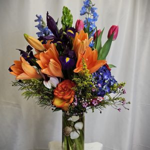 A vibrant bouquet of Orange Tulips and Purple Iris' arranged in a clear vase.