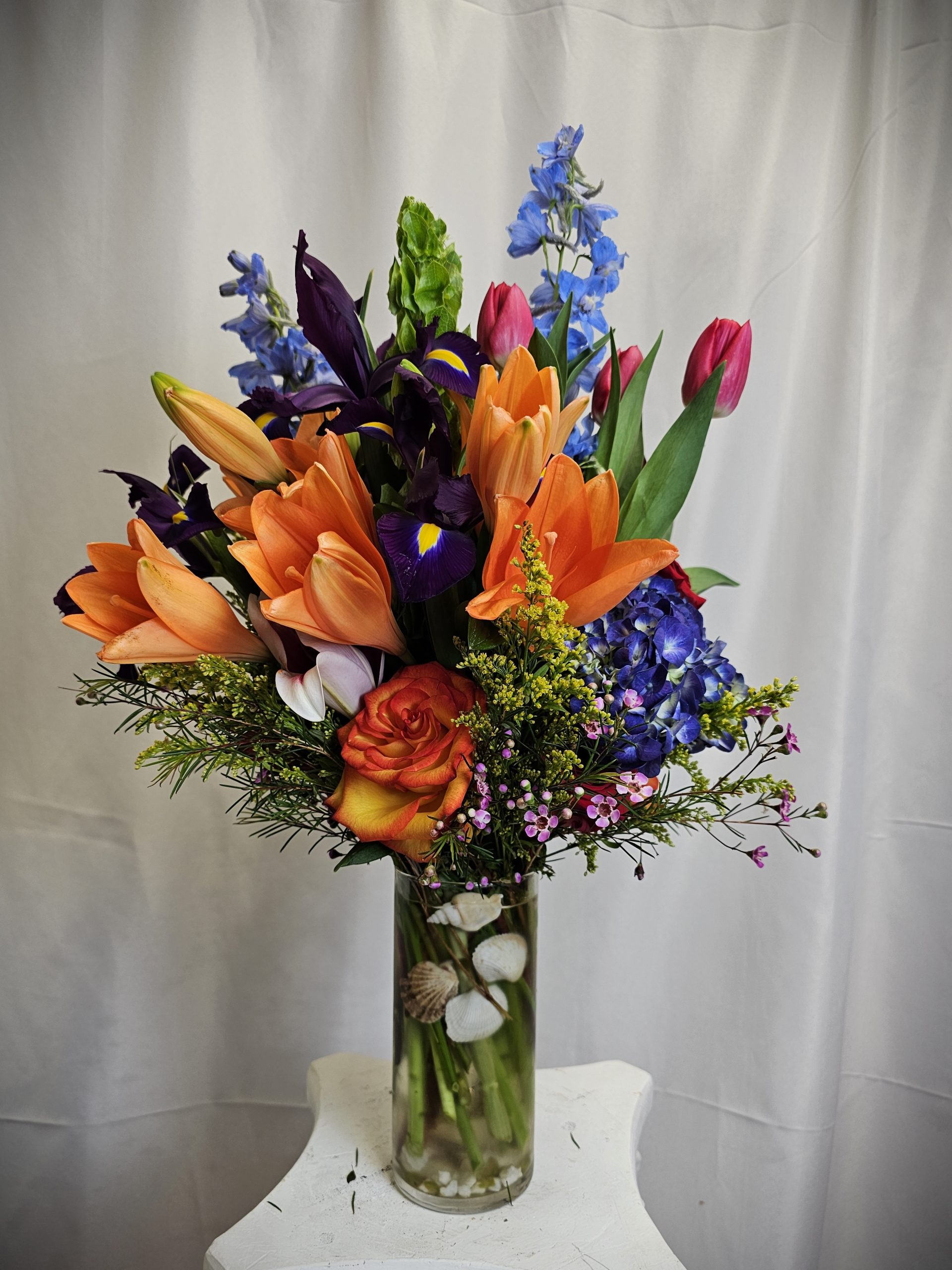 A vibrant bouquet of Orange Tulips and Purple Iris' arranged in a clear vase.