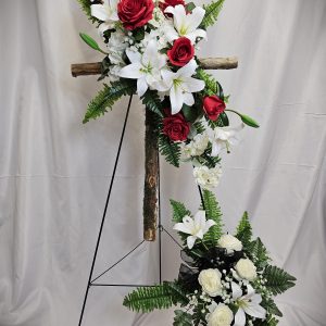 A Wooden Cross & Silk Flowers Easel featuring white lilies, white roses, and red roses, displayed on a wooden cross and stand, against a beige backdrop.