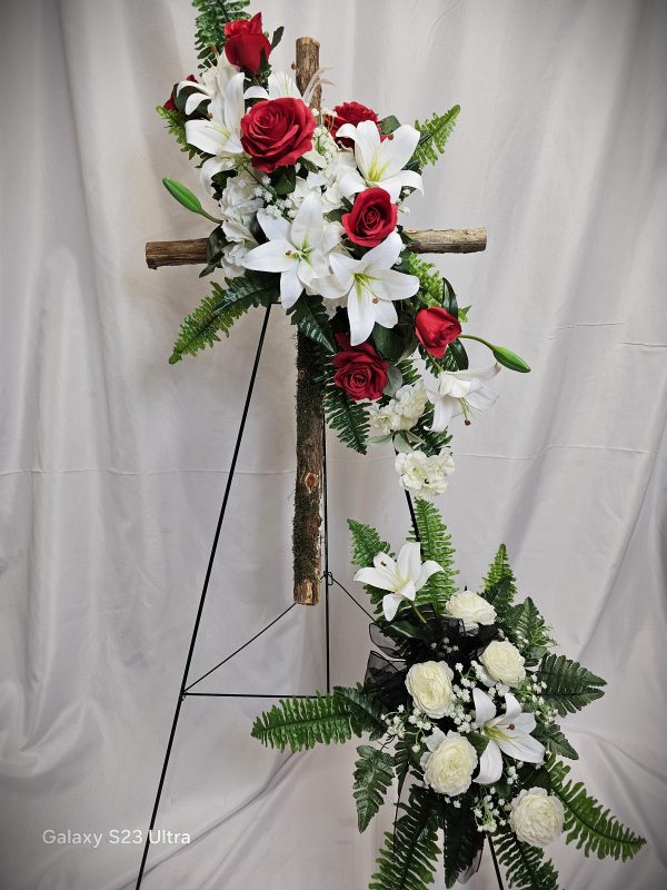 A Wooden Cross & Silk Flowers Easel featuring white lilies, white roses, and red roses, displayed on a wooden cross and stand, against a beige backdrop.