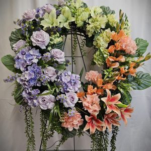 A floral wreath with a mix of purple, orange, and green flowers, including roses, hydrangeas, lilies, and greenery, displayed against a white background.