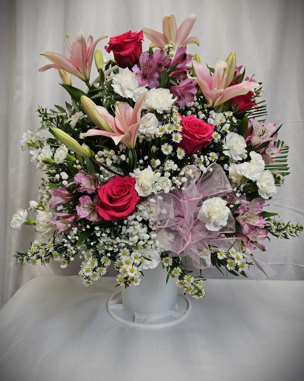 The Mix Sympathy Basket is a beautiful floral arrangement presented in a white vase, featuring an exquisite combination of pink lilies, red roses, white carnations, and baby's breath. A delicate pink ribbon is lovingly tied around the vase, all set against a plain backdrop.