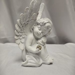 The "Sympathy Angel" figurine, featuring detailed white wings and holding a small, intricately designed gold object in its hands, is set against a smooth cloth background.