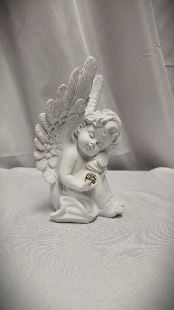 The "Sympathy Angel" figurine, featuring detailed white wings and holding a small, intricately designed gold object in its hands, is set against a smooth cloth background.