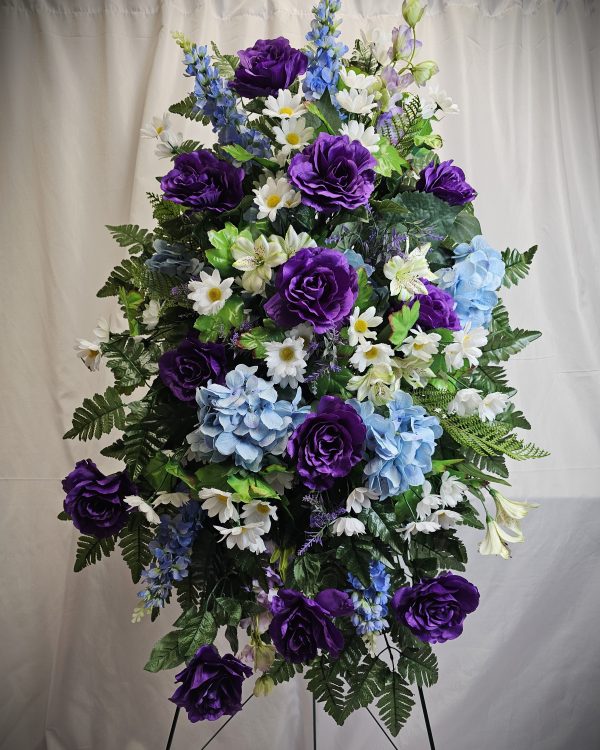 A Fresh or Silk Flower Easel featuring purple roses, blue hydrangeas, white daisies, and green foliage on a stand against a white background.