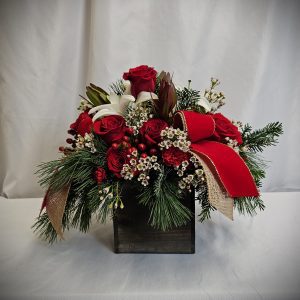 The Wooden Christmas Box Arrangement features a stunning floral design with red roses, white lilies, greenery, and decorative red bows in an elegant wooden box placed against a white background.