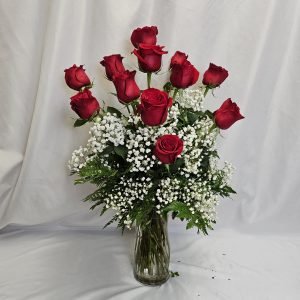 A half dozen red roses and white baby's breath in a clear glass vase, set against a plain white background. Product Name: Valentine Special: Half Dozen Roses.