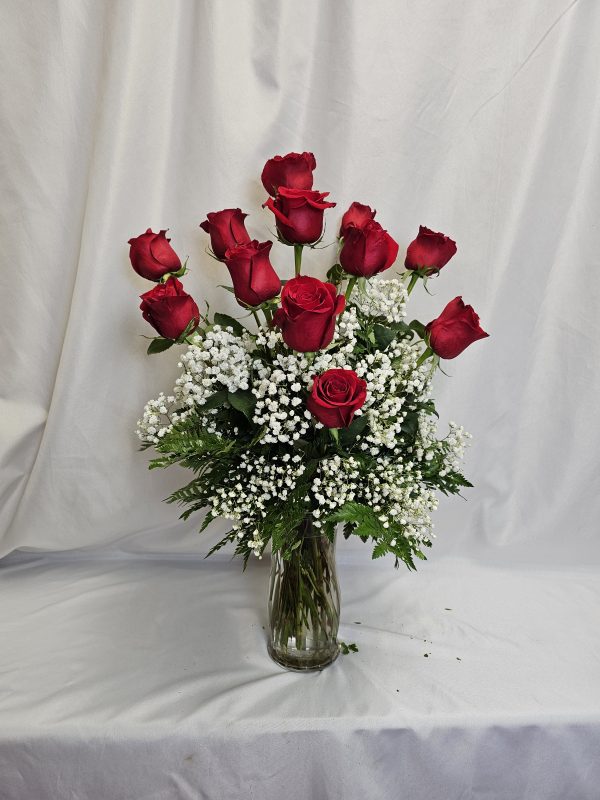 A half dozen red roses and white baby's breath in a clear glass vase, set against a plain white background. Product Name: Valentine Special: Half Dozen Roses.